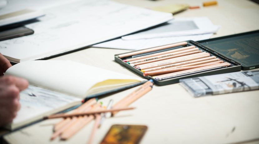 Sketchbooks and pencils are scattered over a desk. 