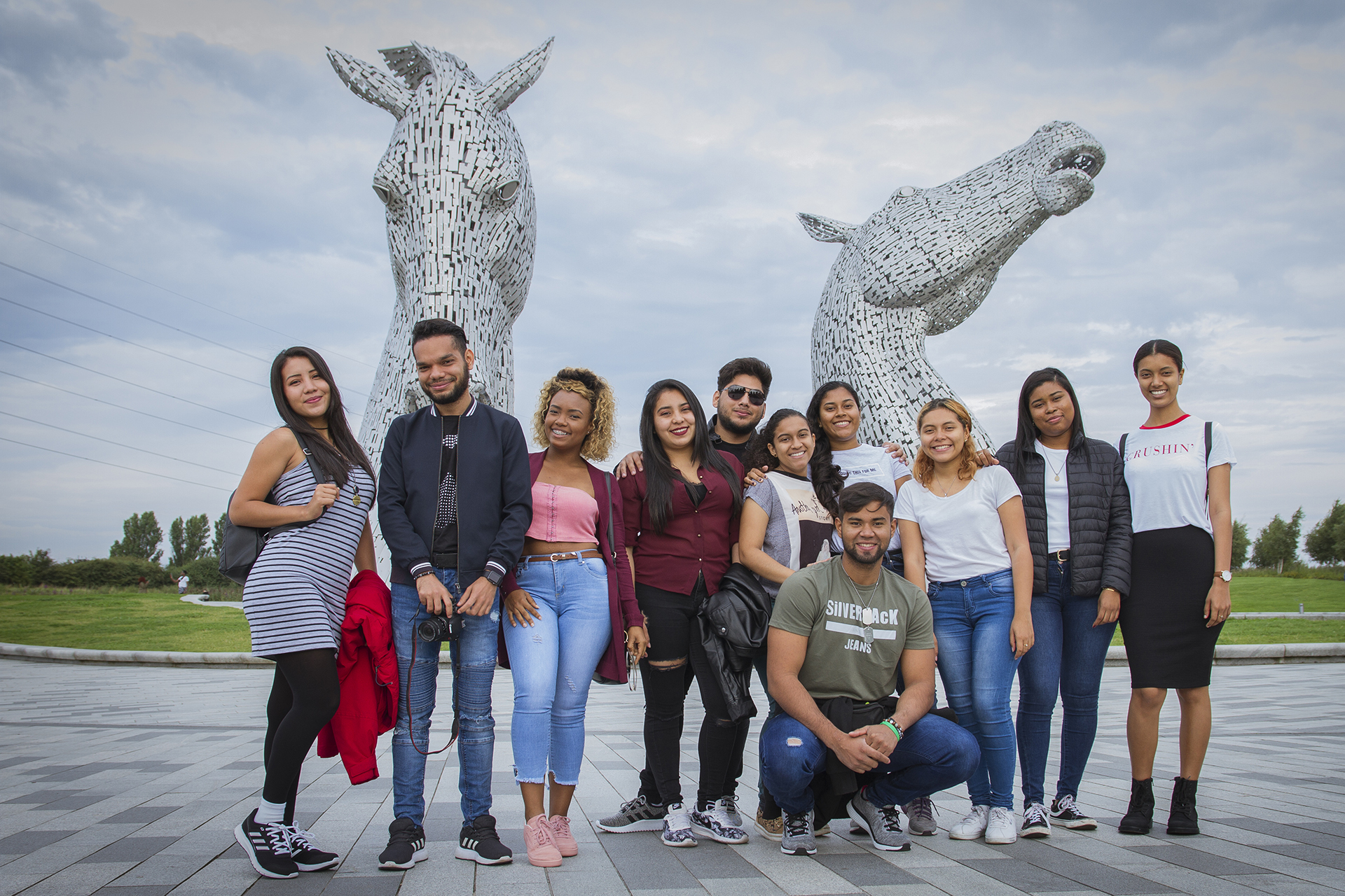 Group of students on a social programme standing for a group photo at the Kelpies, which are a large metal horse structure.