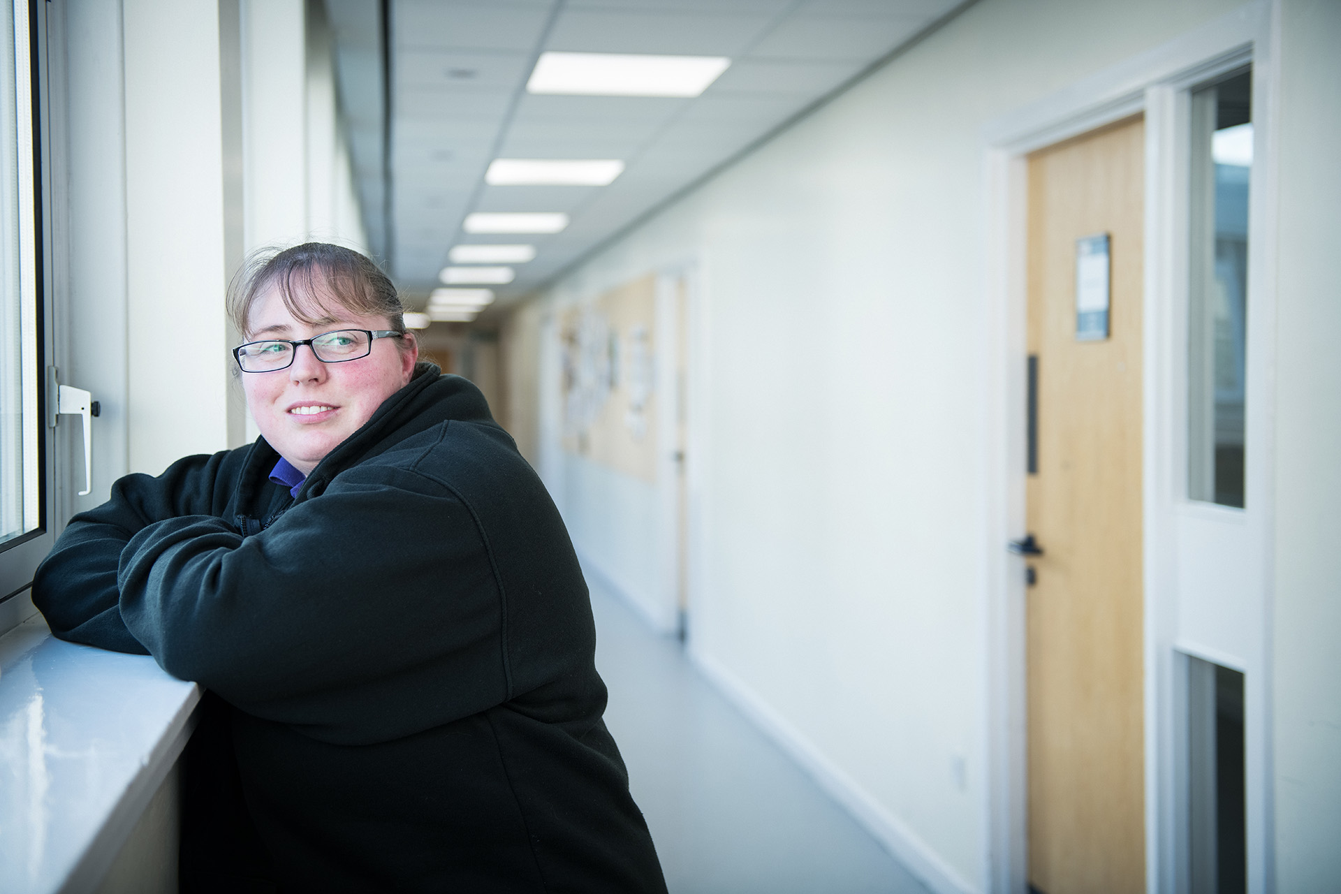 Smiling student leaning on a windowsill in a corridor.