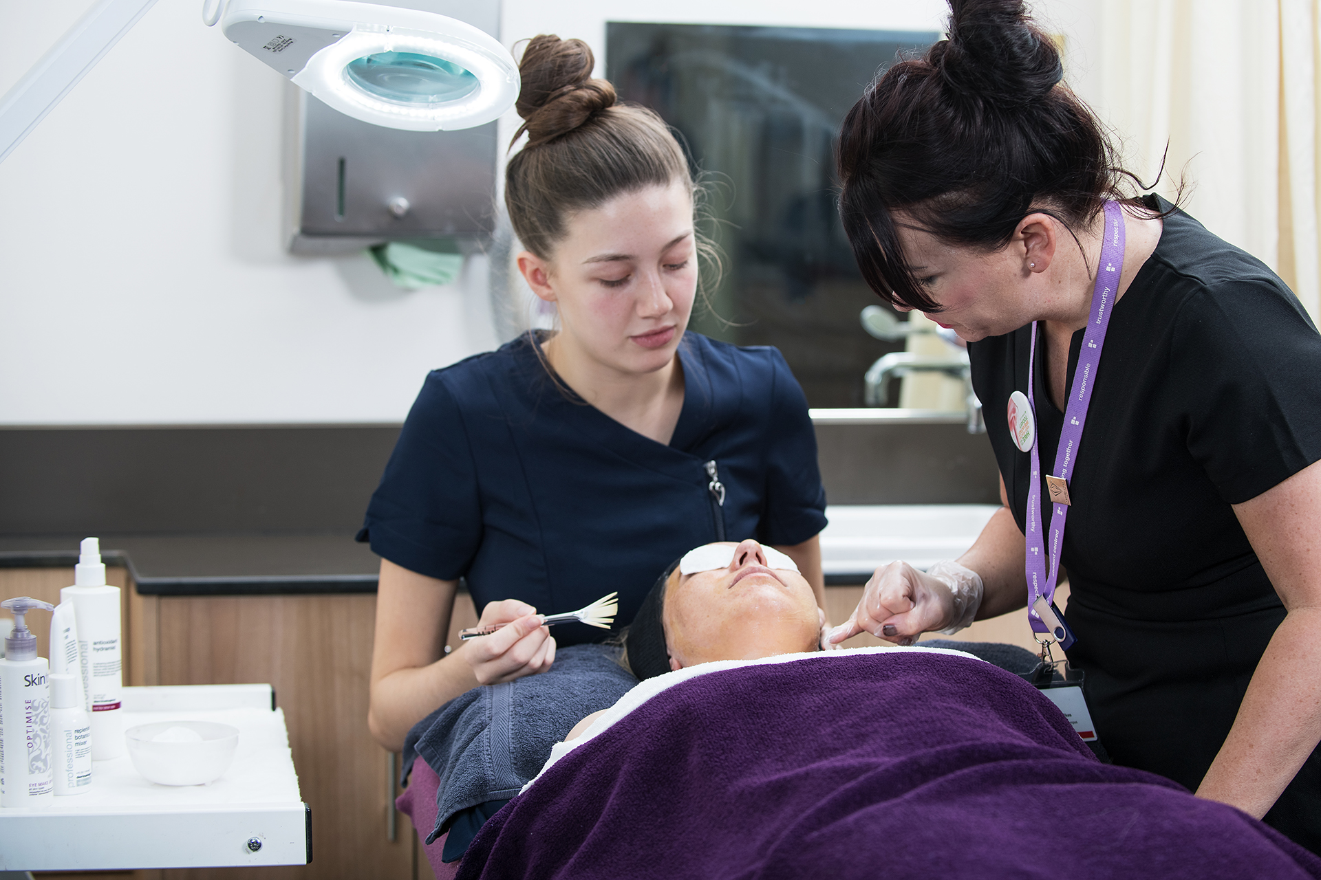 Beauty student giving a client a facial in the salon while a lecturer observes. 