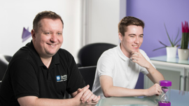 Young student working at a desk in an open plan office during a work placement next to their mentor.