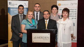 A group of six individuals posing for a photo, standing in front of a banner, with a podium in the foreground.
