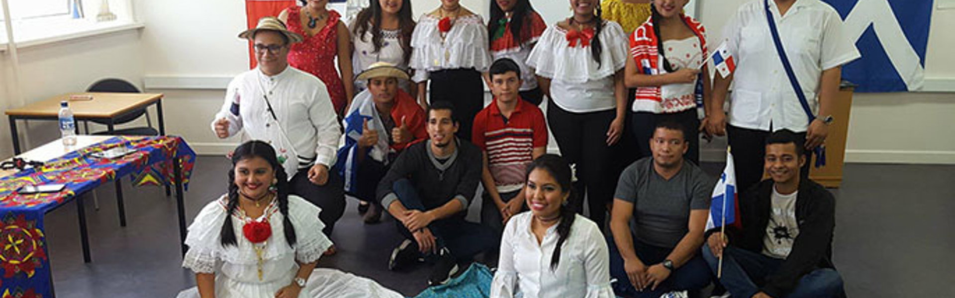 A group of individuals in colorful traditional clothing poses together in a room, showcasing cultural pride and community spirit.