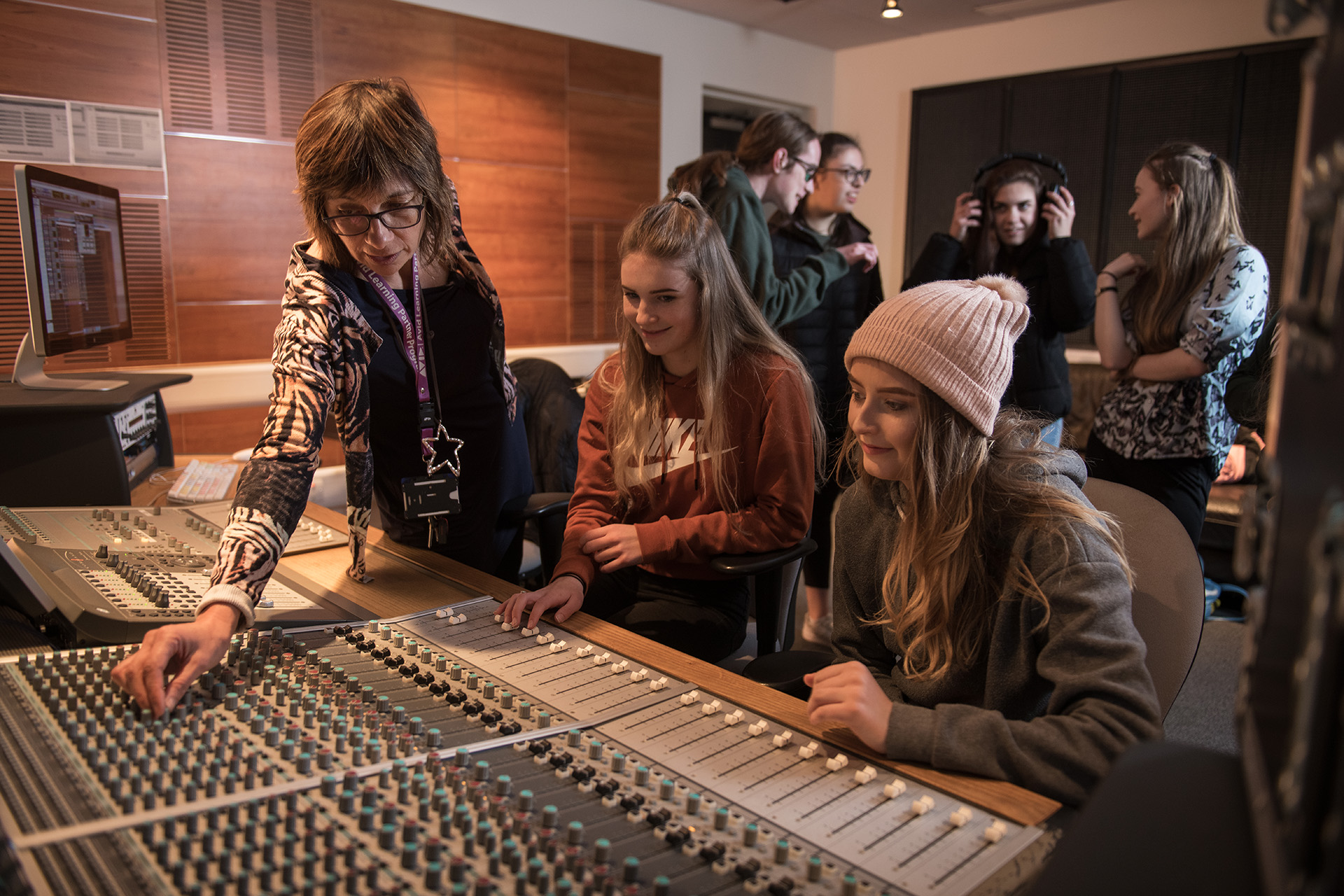 Sound production lecturer showing two young students how to work equipment.
