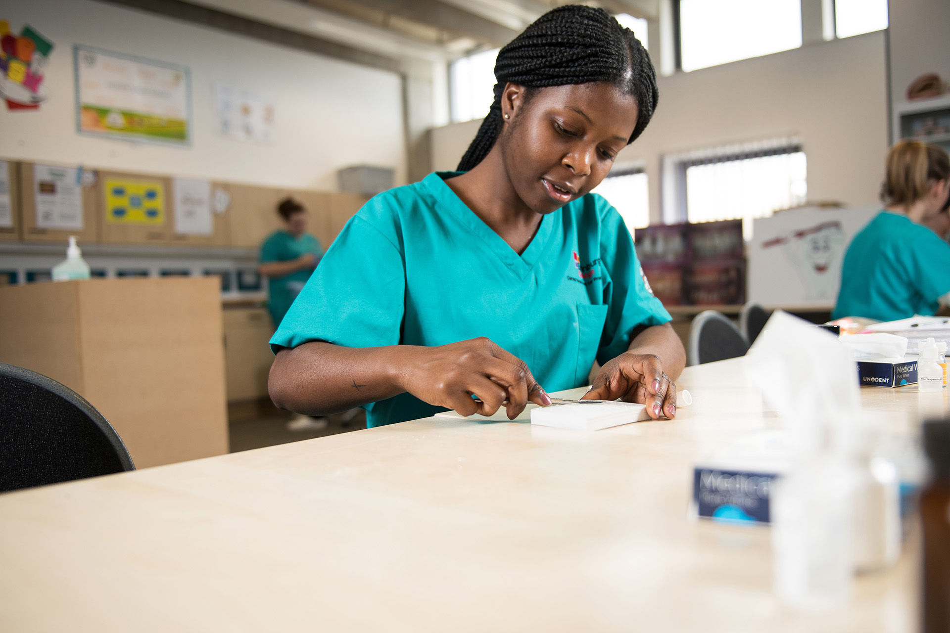 Dental student wearing blue scrubs working with dental tools at a desk.